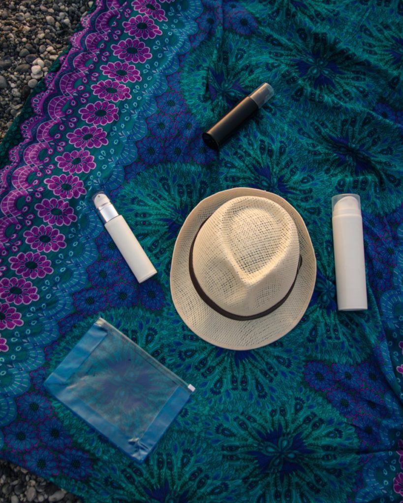 A beach towel with sun protective lotions and a hat on top