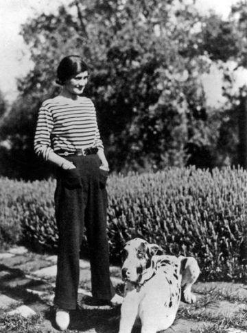 The History of Beach Umbrellas: Historic photo of Coco Chanel during summer vacation in France ready to sit under beach umbrella