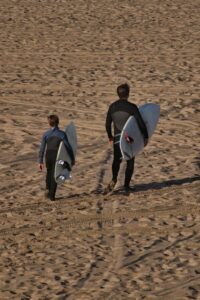Father son carrying surf boards on the sand