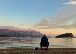 man in black jacket sitting on red and white fishing rod during sunrise